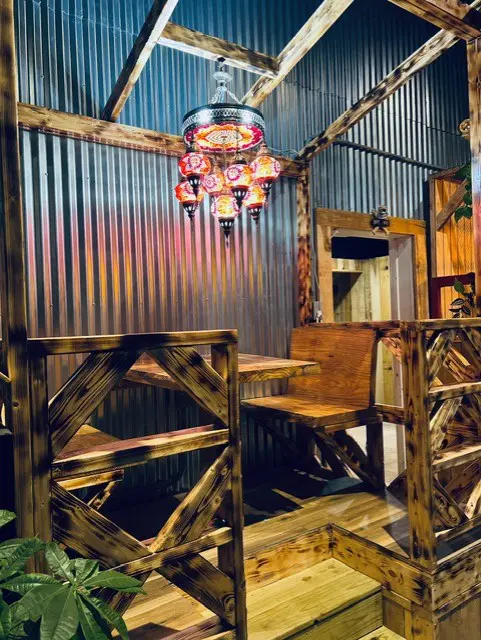 Rustic wooden dining booth with corrugated metal walls and a colorful mosaic Turkish chandelier hanging above the table