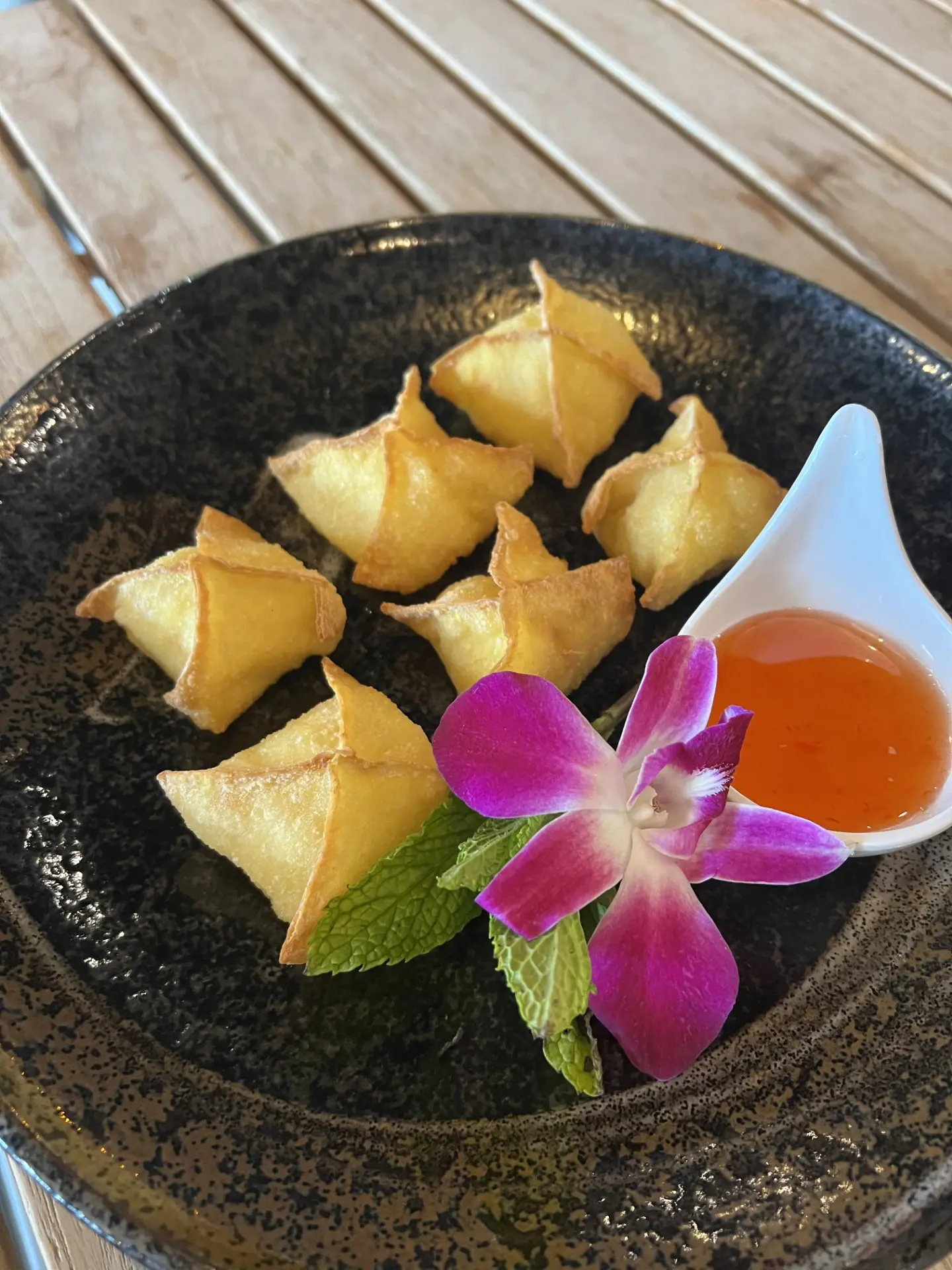 Golden fried Thai crab rangoons arranged on a black plate with sweet chili dipping sauce, a sprig of mint and a purple orchid garnish — tiki bar appetizer at MPM Tiki Bar in Short Pump, Richmond